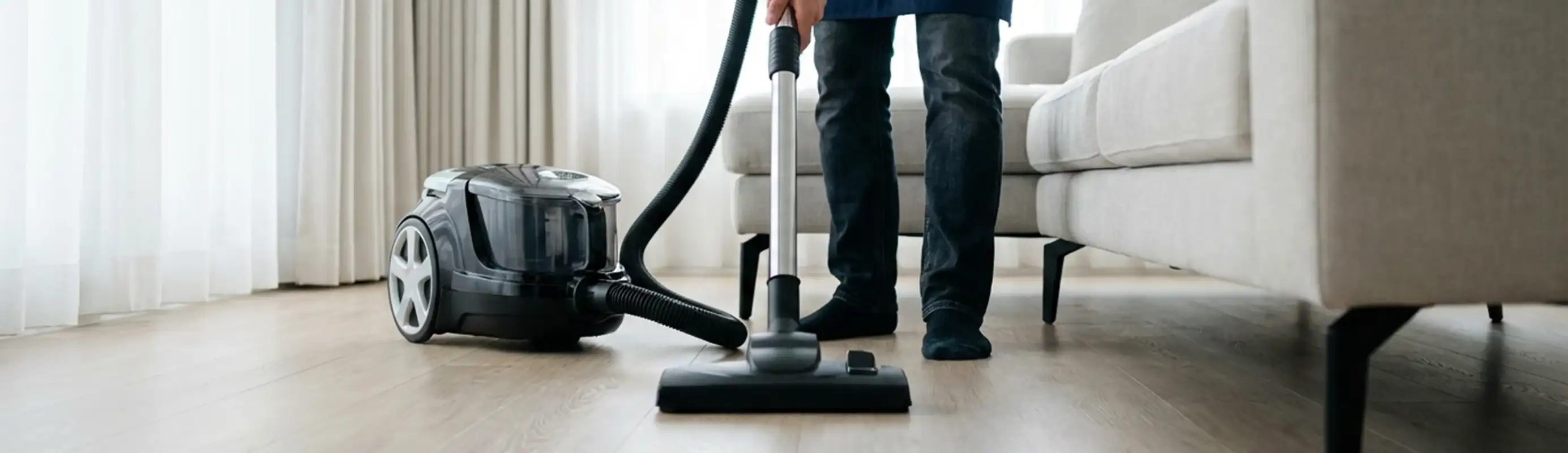 Professional house cleaner vacuuming a living room floor with a canister vacuum cleaner, Birmingham, AL.
