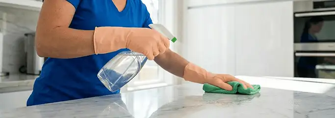 Maid service worker spraying and wiping a kitchen countertop with a microfiber cloth for sanitizing, Birmingham, AL.