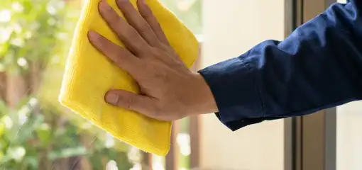 House cleaner wiping a glass window with a yellow microfiber cloth for streak-free cleaning, Birmingham, AL.